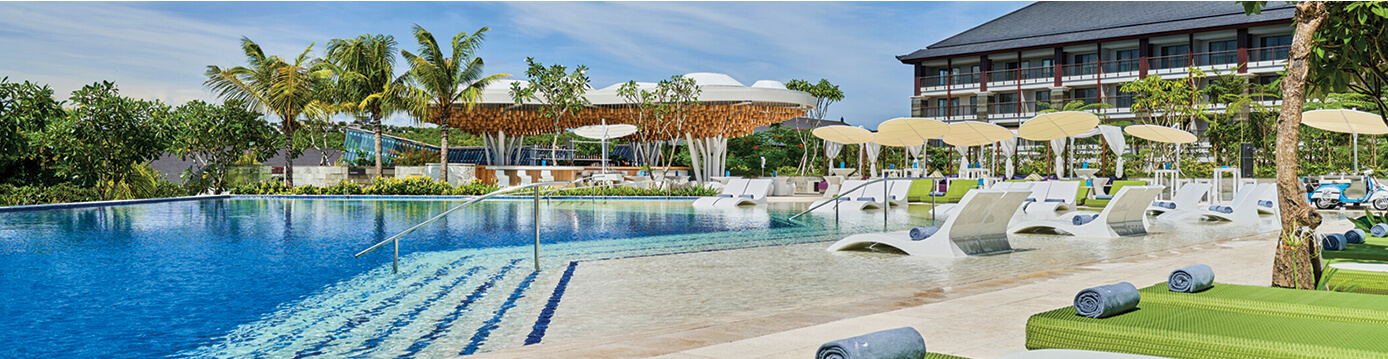 Shimmering blue resort pool surrounded by deck chairs, sun umbrellas, and tropical palm trees