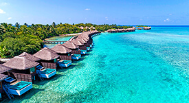 Aerial view of lush tropical island with thatched-roof bungalows overlooking a bright blue shimmering sea