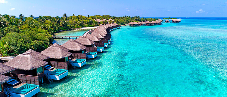 Aerial view of lush tropical island with thatched-roof bungalows overlooking a bright blue shimmering sea